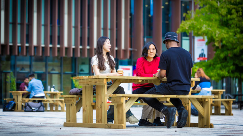 Students sitting on a bench in Centenary Square on Leicester campus.