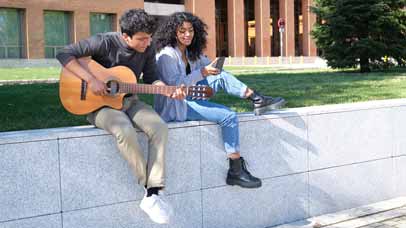 A student playing a guitar whilst another listens on university campus