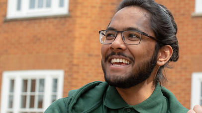 student in a green jumper smiling in front of some houses