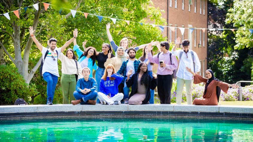 A group of students on the University of Leicester campus, some of them have their arms in the air