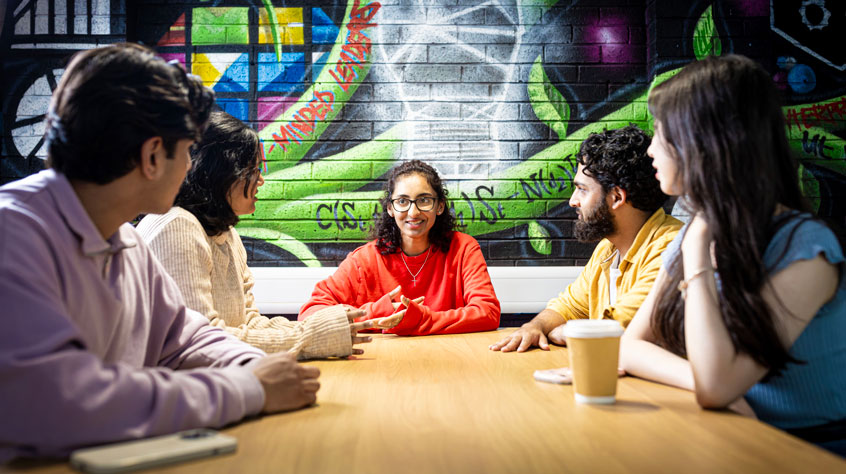 Students sitting around a table drinking coffee and talking.