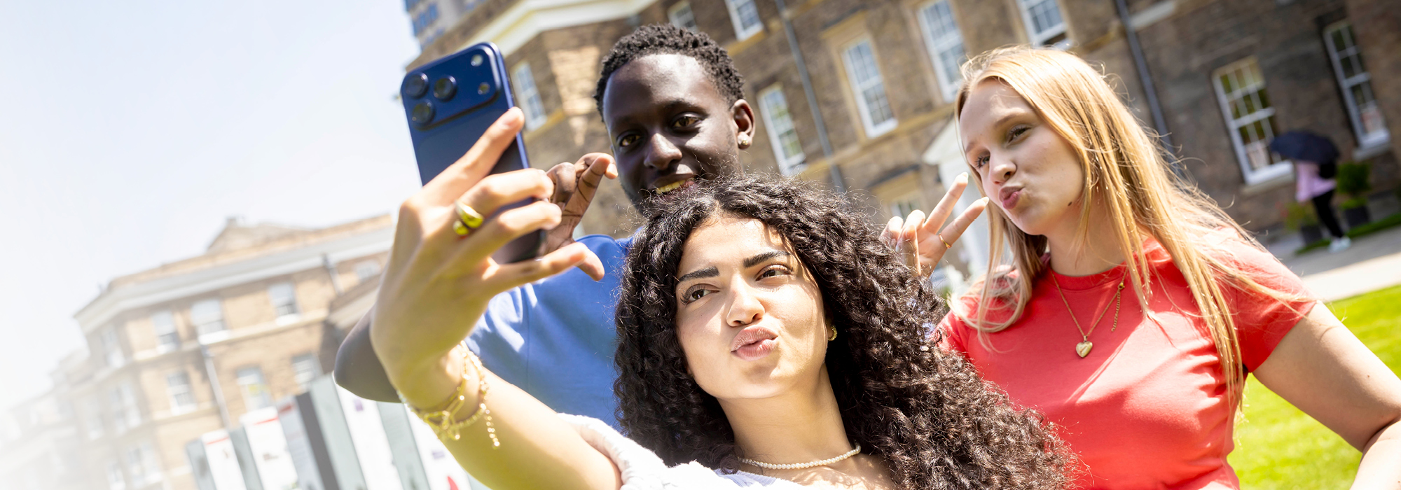 Three students taking a selfie outside, on a sunny day.