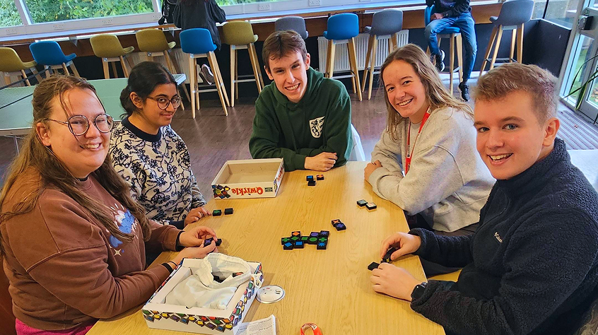 Five students sitting around a table, playing a board game.