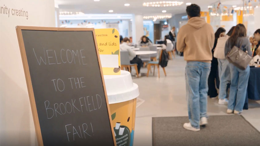 Blackboard stating 'welcome to the Brookfield Fair!' and people walking to the right of the board.