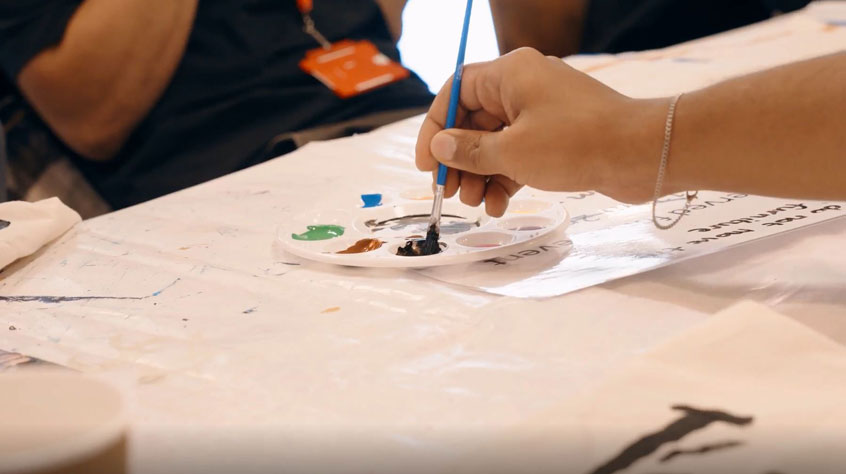 Close up of a person's hand dipping a paint brush into a paint palette.