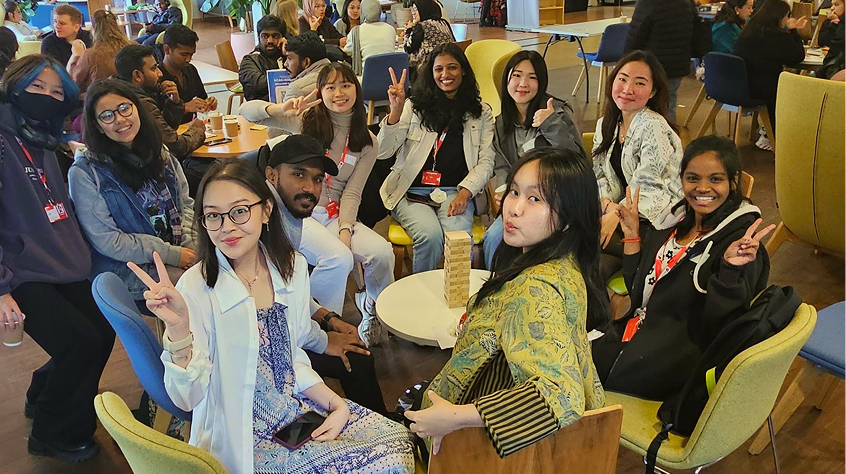 Group photo of students at a social event, playing jenga around a table.