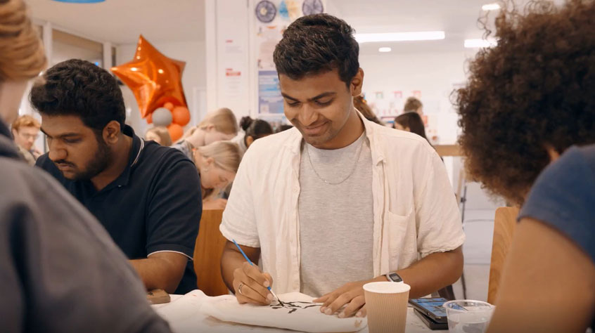 A group of individuals seated at tables, engaged in painting in a collaborative setting.