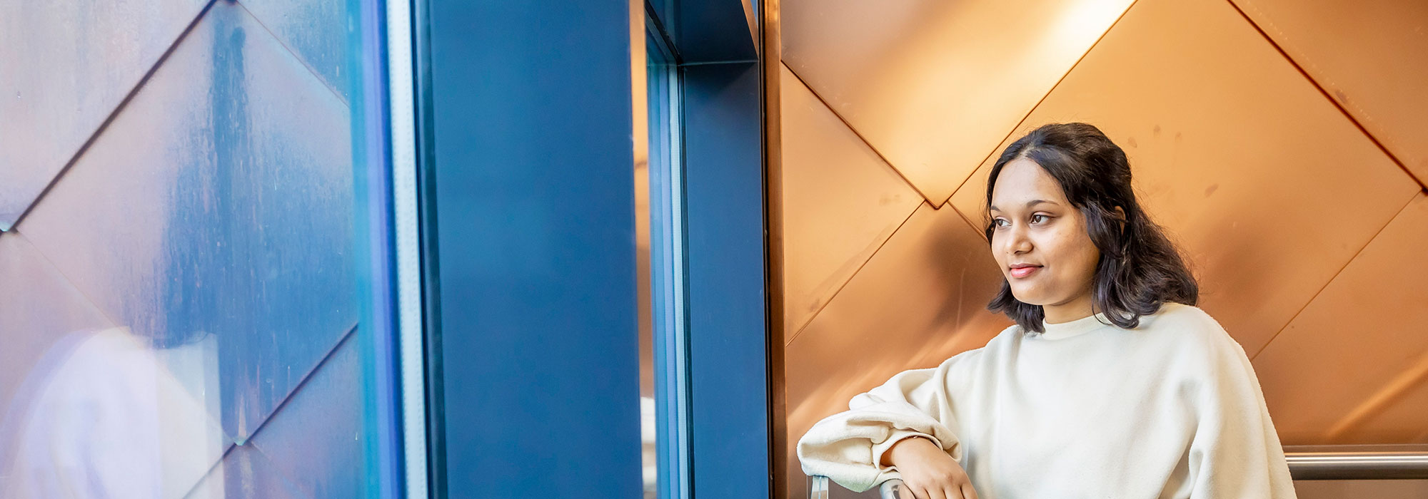 Photo of a female student leaning against a balustrade and looking into the distance 