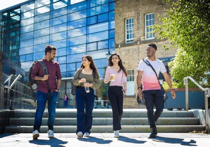 Four smart looking students walking in a line through the University of Leicester's leafy city campus on a sunny day