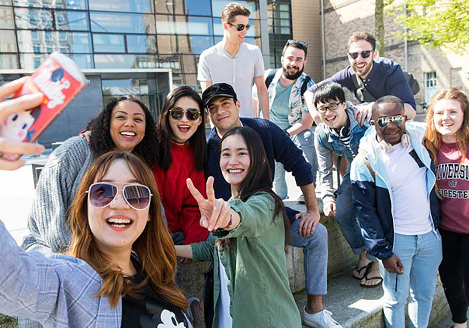A group of students on Leicester University campus smiling and laughing, while taking a selfie