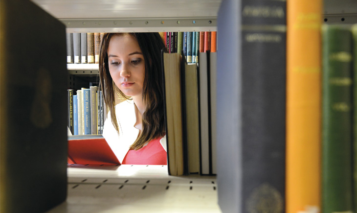 Student reading a book viewed through bookcase